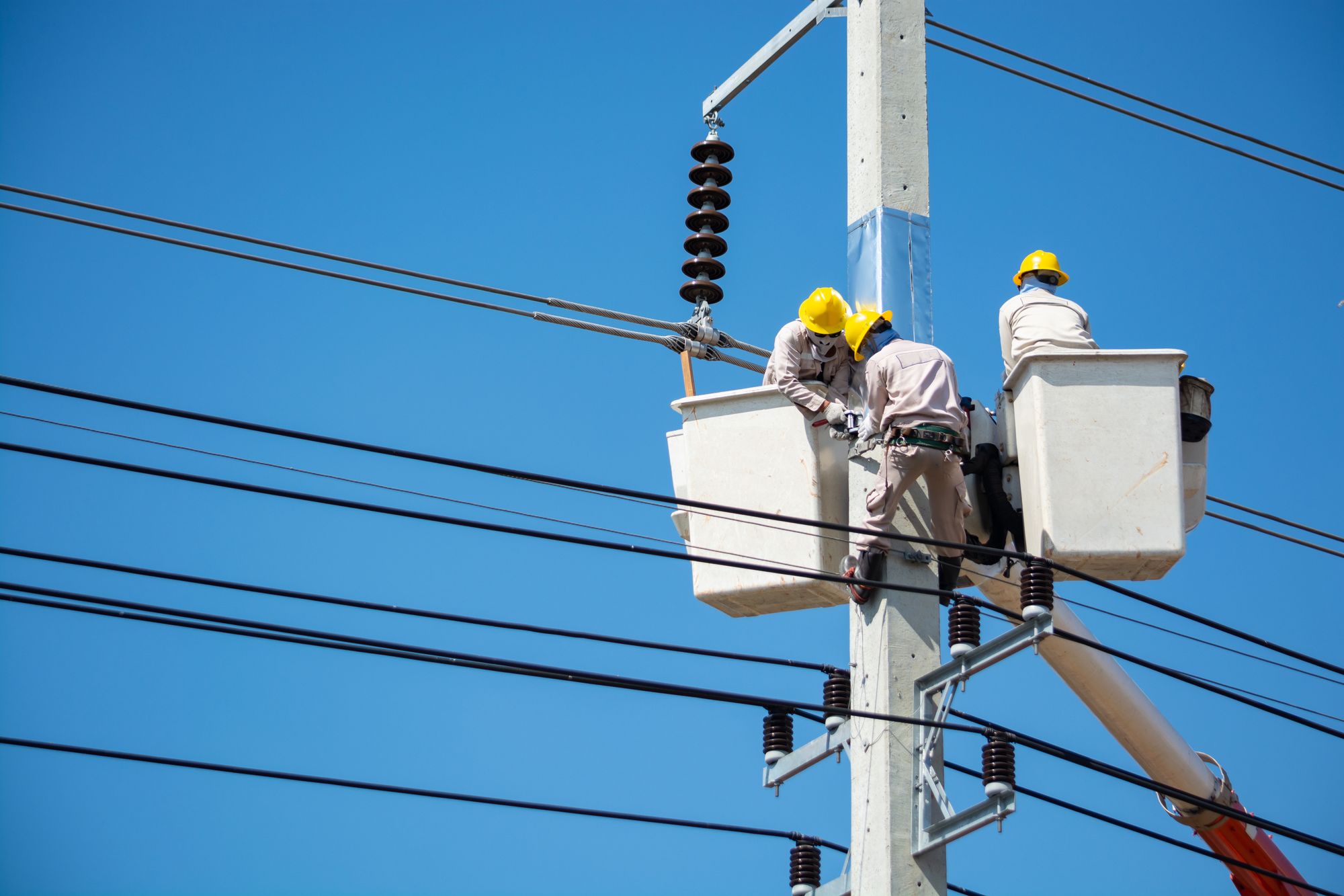 Elektromonteure bei Arbeiten an einer Freileitung vor blauem Himmel